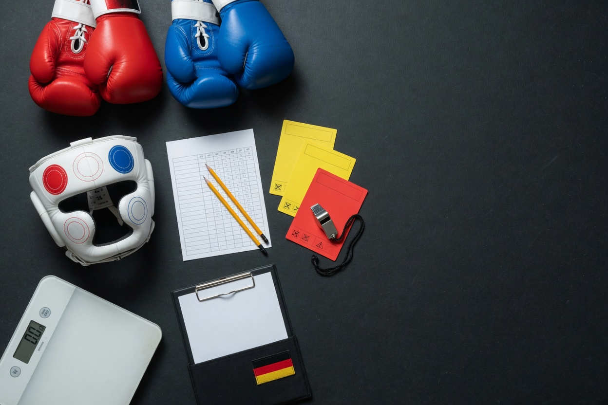 Flat-lay photo of boxing gloves, headguard, scorecard, foul cards with whistle, and a digital